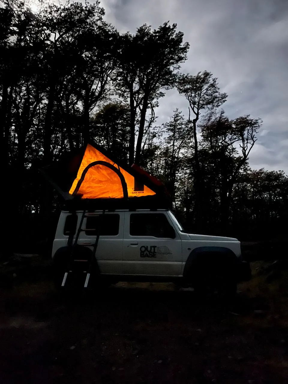 Silueta del camper con la carpa rooftop iluminada, de noche